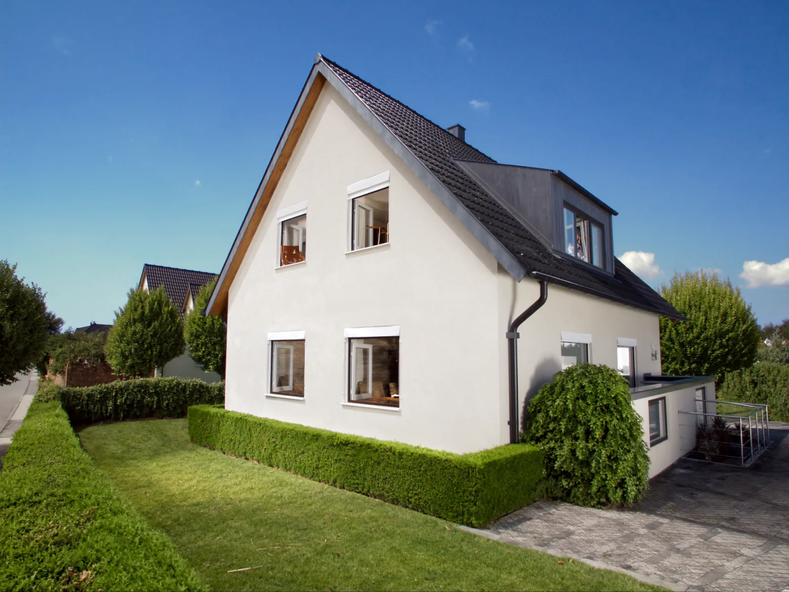 Gepflegtes Einfamilienhaus mit Satteldach in einer deutschen Wohnstraße an einem sonnigen Frühlingsmorgen